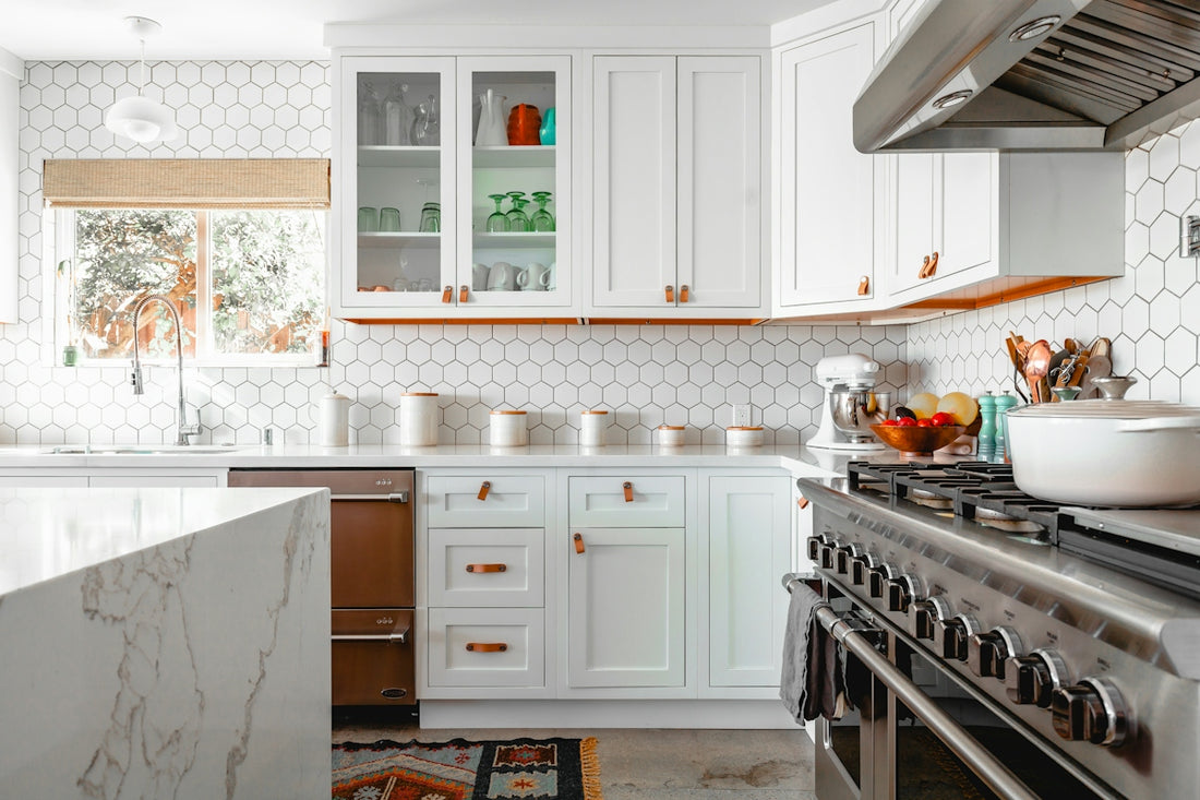A bright kitchen with white cabinets, hexagonal wall tiles, and a marble island